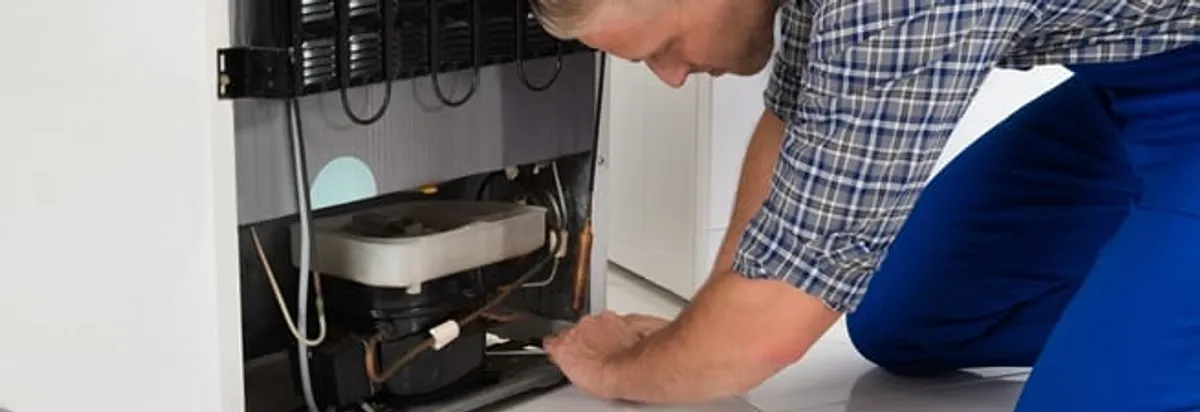 Refrigerator repair technician servicing the compressor and condenser area in Eugene, OR